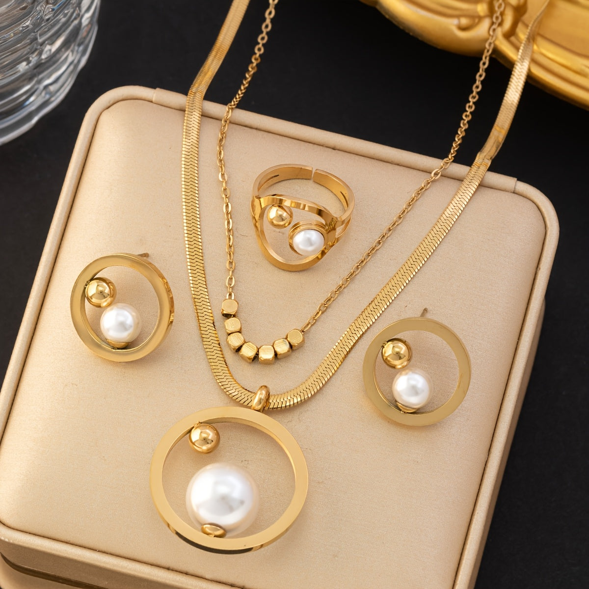 Um conjunto elegante de quatro peças com um colar, brincos e anel em aço inoxidável dourado, perfeito para mulheres usarem diariamente, em encontros ou como presente.